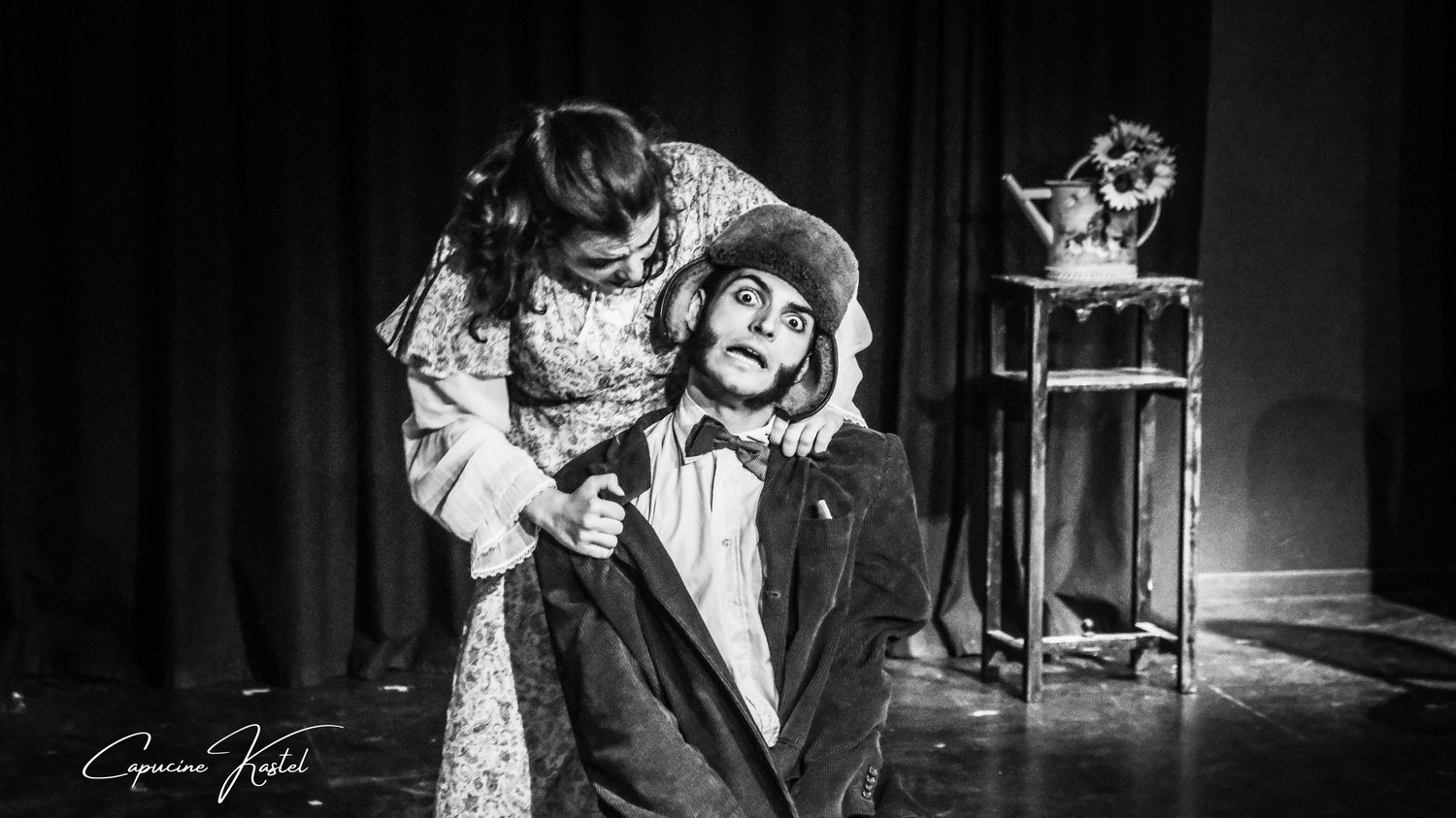 Une comédienne penchée sur un comédien grimé en clown, coiffé d'un chapeau.